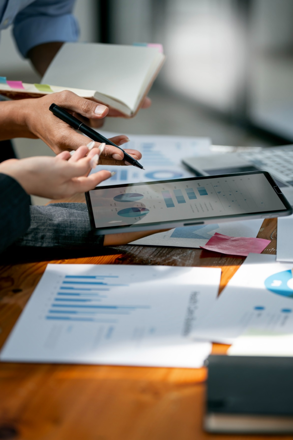 Hands of business people pointing and discussing charts and graphs on printed reports at a desk.