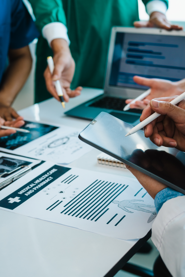 Hands of business people pointing and discussing charts and graphs on printed reports at a desk.