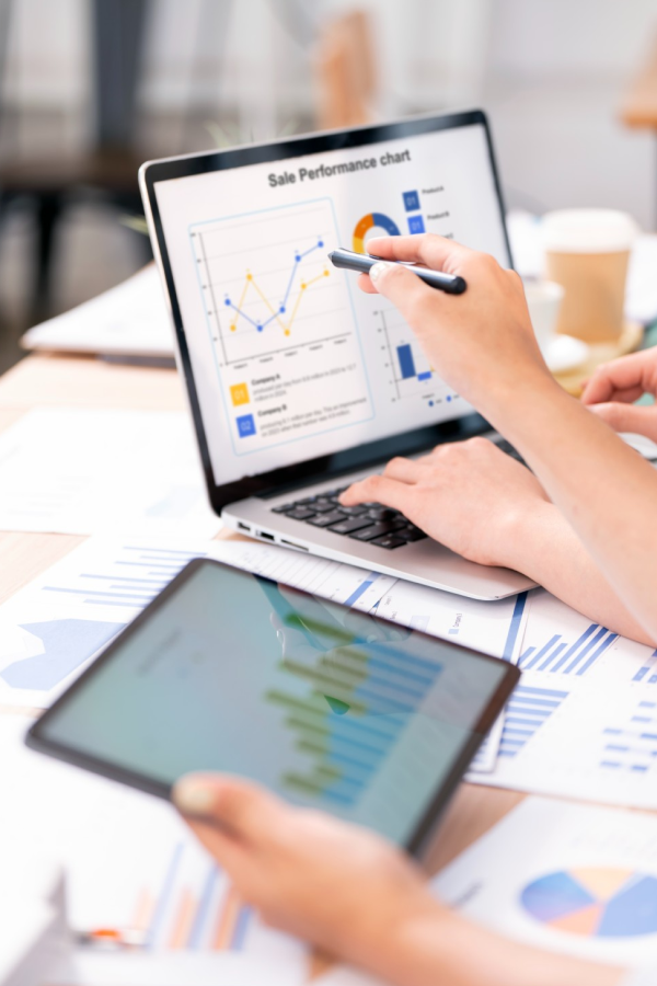 Hands of business people pointing and discussing charts and graphs on printed reports at a desk.