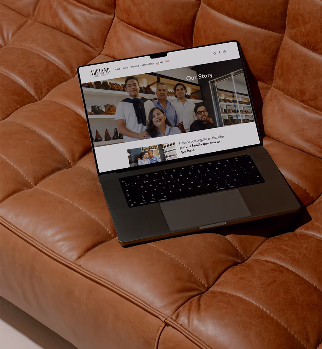 Laptop on a brown leather couch displaying a family photo and text on a website about a shoe brand named Adriano.