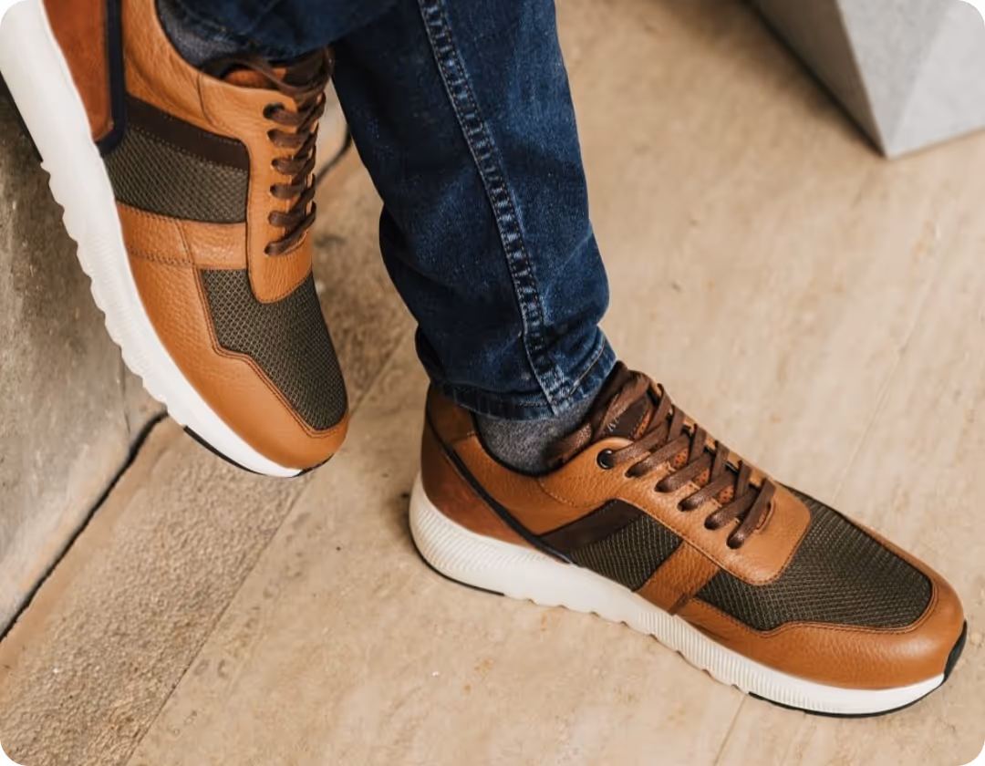 Person wearing brown and dark green casual sneakers with white soles and blue jeans.