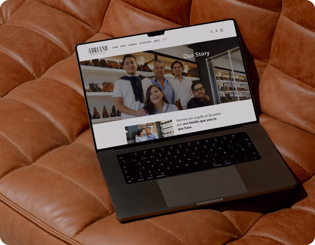 Open laptop on brown leather couch displaying Adriano footwear website with a family photo and text 'Our Story'.