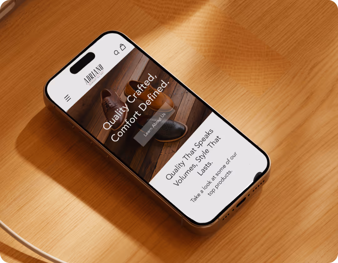 Smartphone on a wooden surface displaying a webpage with text about quality-crafted shoes and a Learn About Us button.