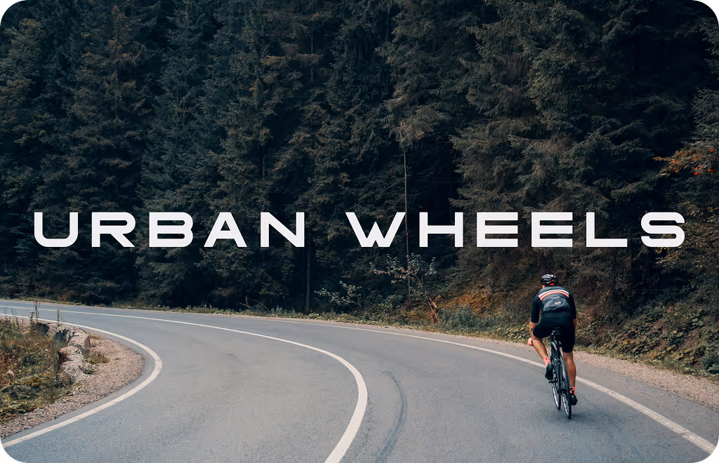 Cyclist riding on a winding road surrounded by dense forest with the text 'URBAN WHEELS' overlayed.