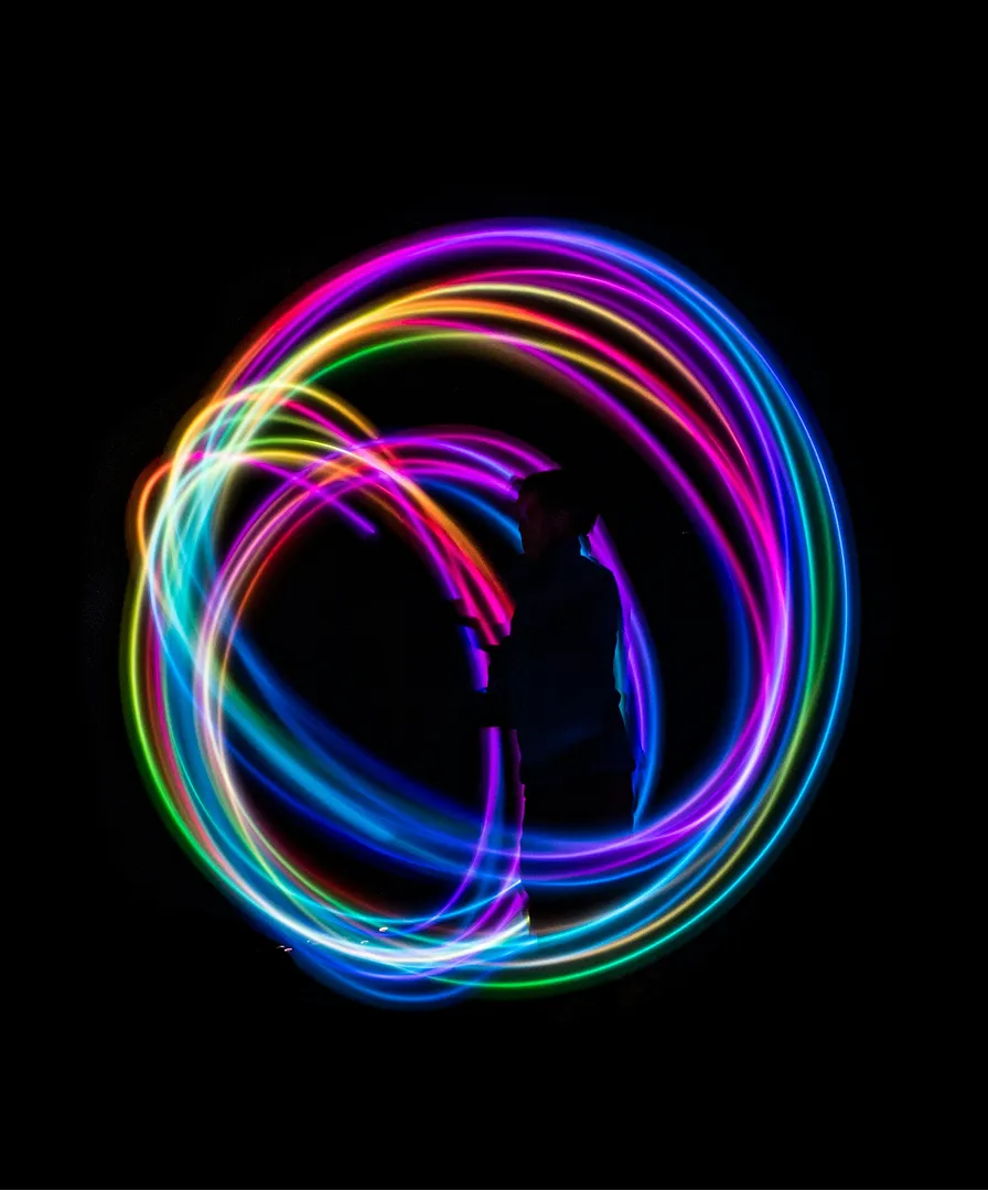 Silhouette of a person spinning colorful light trails forming circular patterns against a black background.