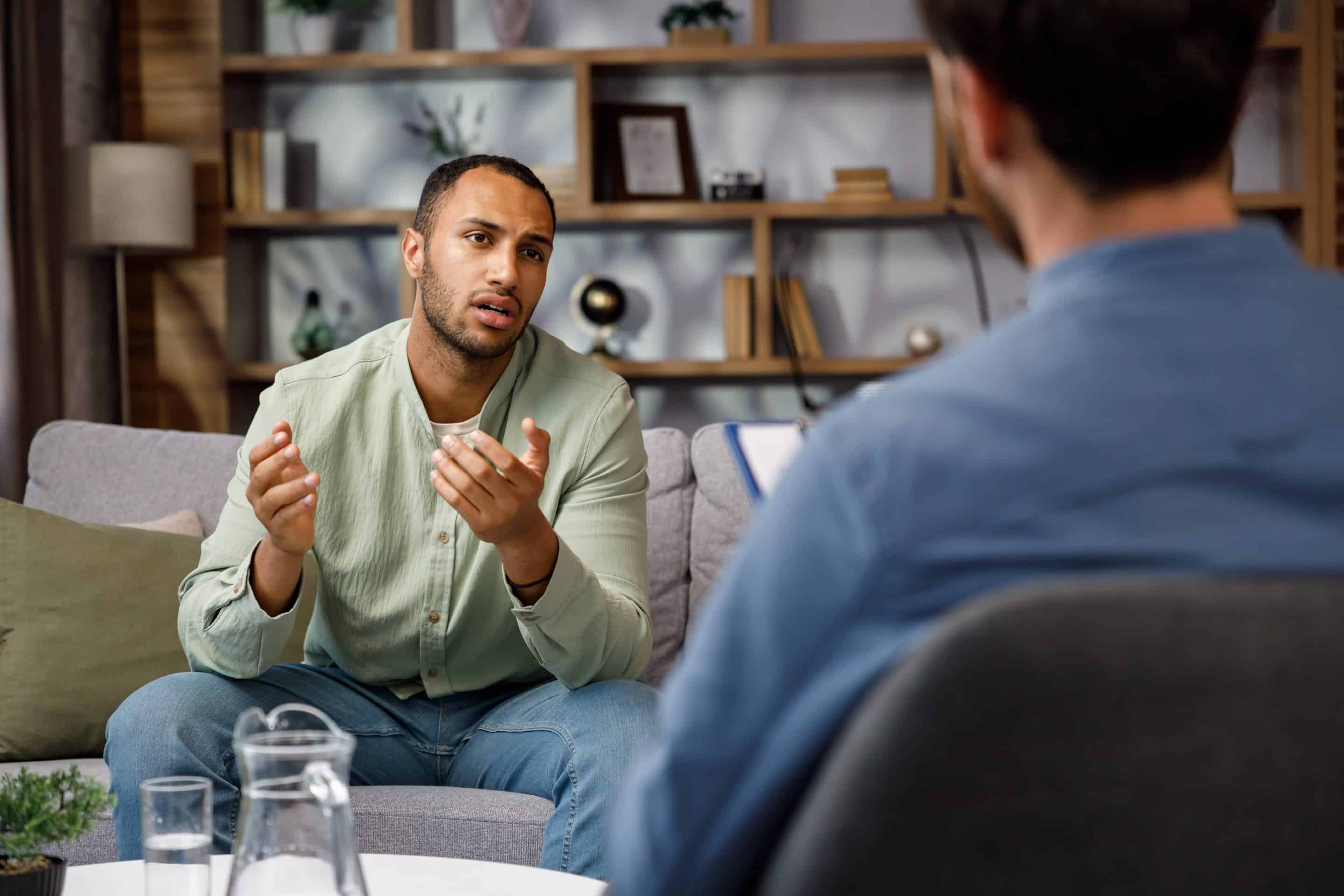 Visiting a psychologist Afro-american man is sitting on the couch and talking to a psychotherapist. He thanks the doctor and smiles, therapy helped him. Help of a psychologist.
