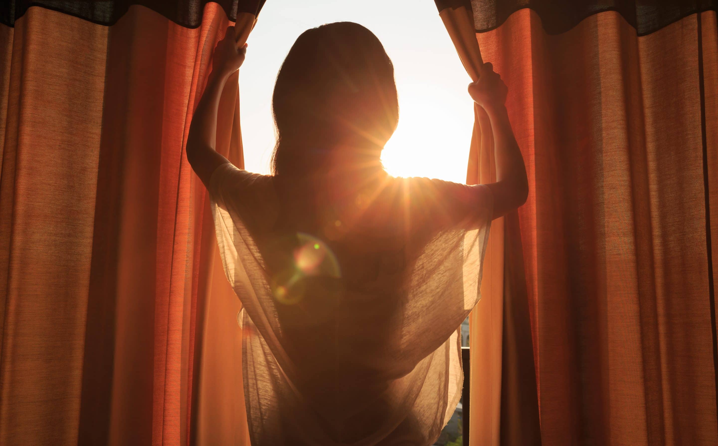 woman opens curtains to reveal sunlight