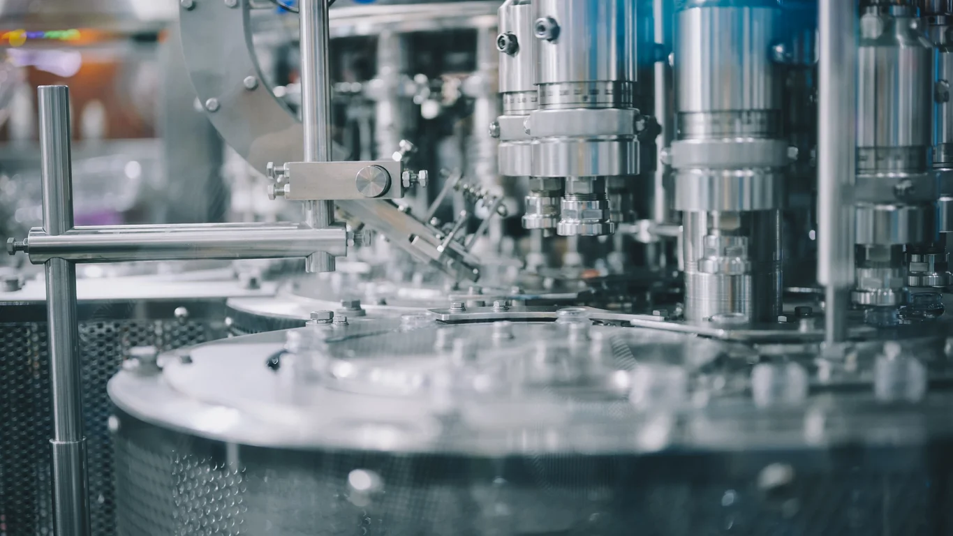 Close-up of an automated stainless steel manufacturing machine with precision mechanical components operating in a modern production facility.