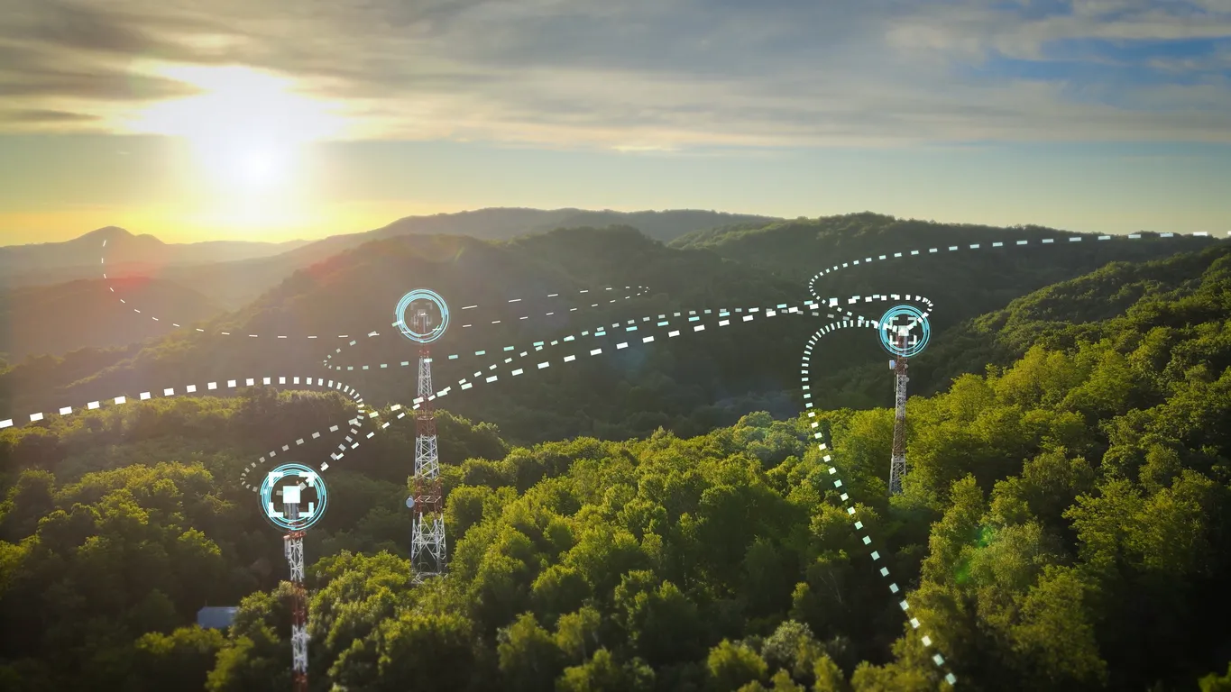 Wireless communication towers transmitting data signals across a forested landscape at sunrise, symbolizing connectivity, digital networks, and sustainable technology integration.