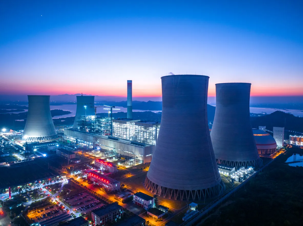 Aerial view of a power plant with large cooling towers and illuminated industrial buildings at dusk, symbolizing energy production and infrastructure.