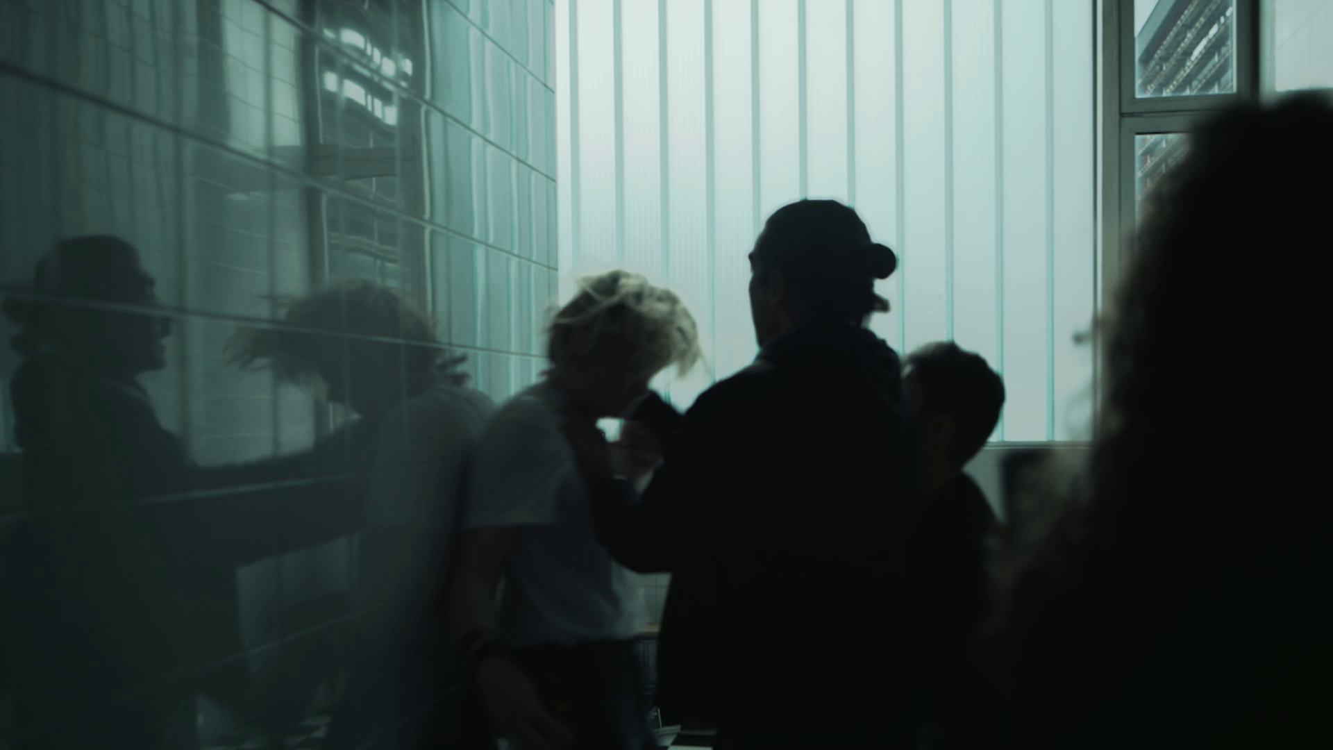 A tense scene with one person holding another against a tiled wall in a dimly lit space.