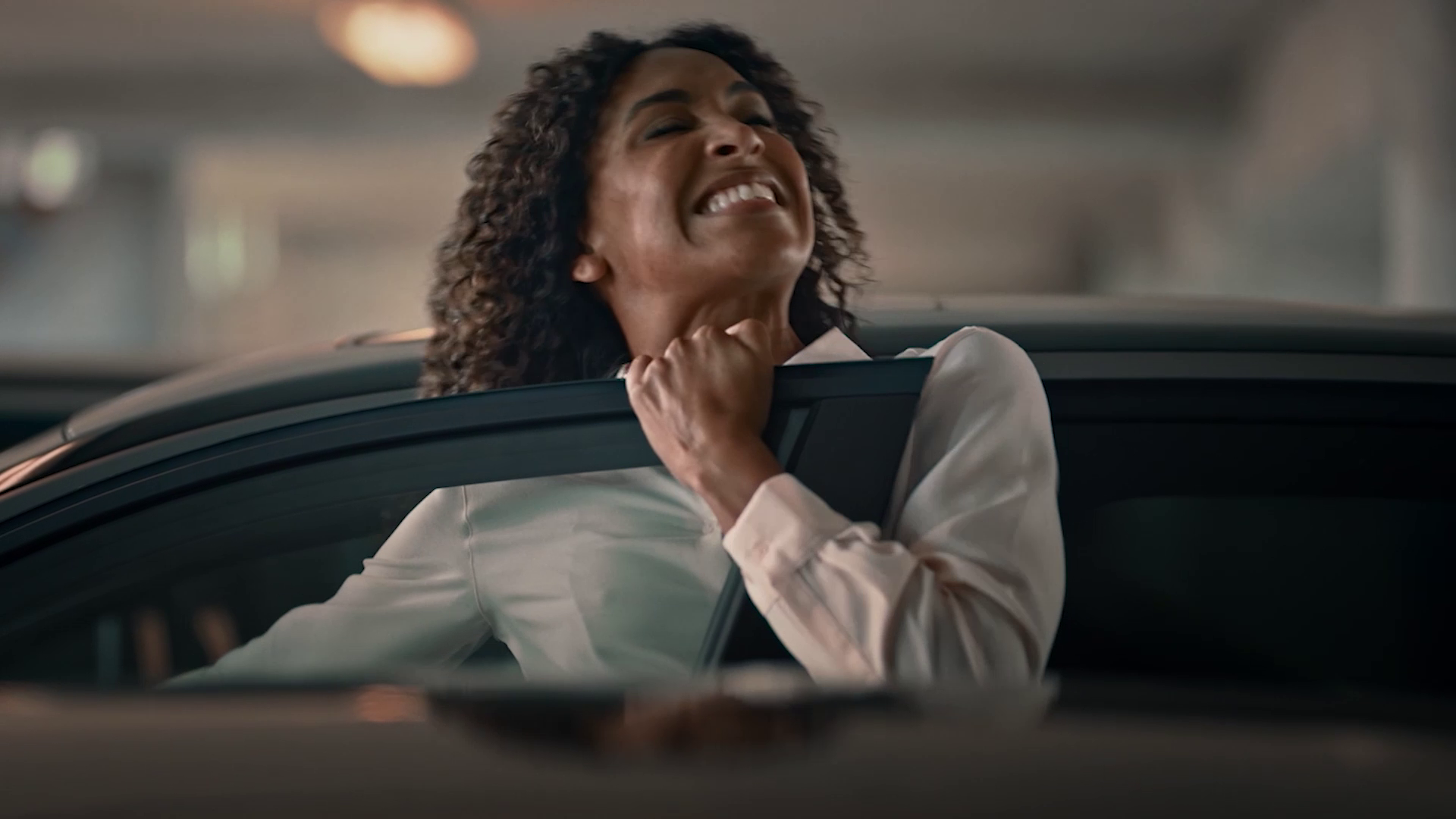 Woman smiling with eyes closed while holding onto a car door frame.