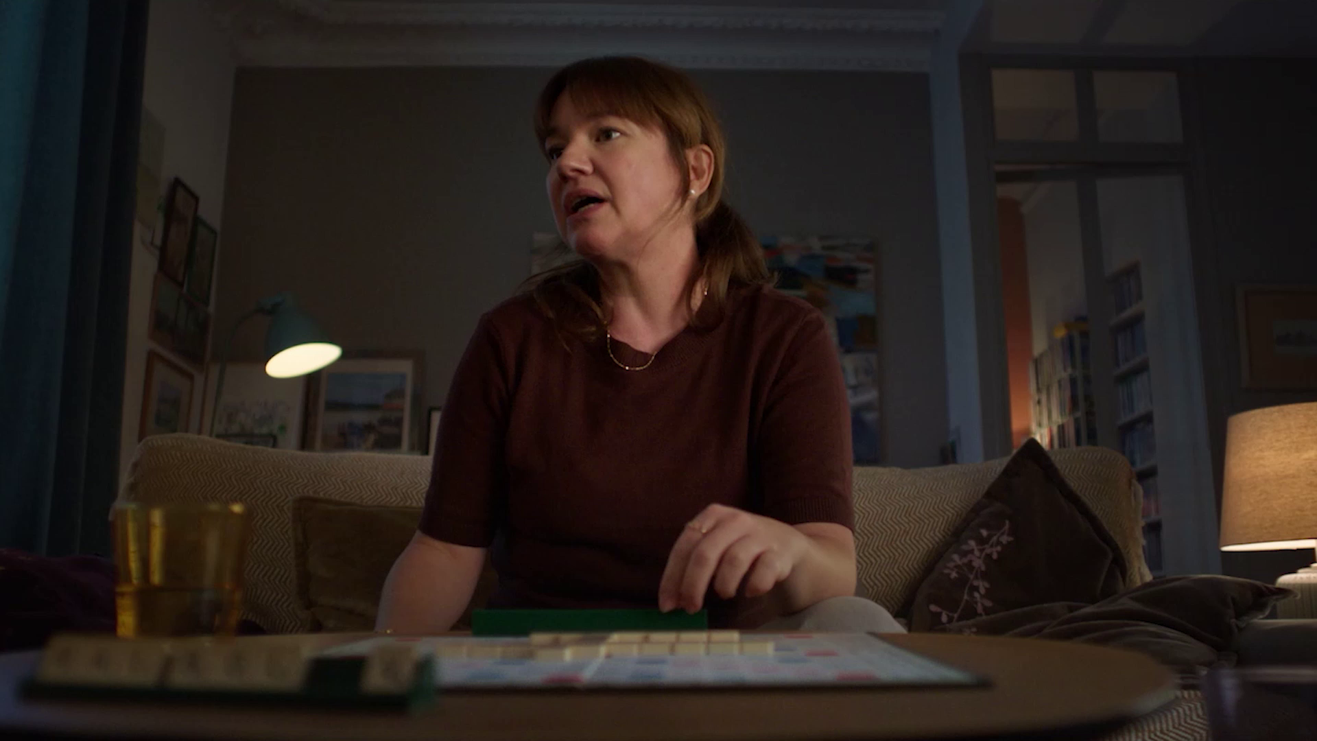 Woman sitting on a couch playing Scrabble in a dimly lit living room.