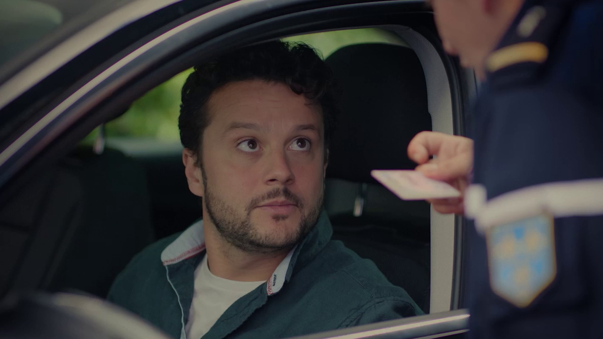Man in a car handing his identification card to a police officer outside the vehicle window.