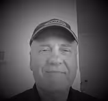 Black and white headshot of a middle-aged man wearing a baseball cap, smiling slightly.