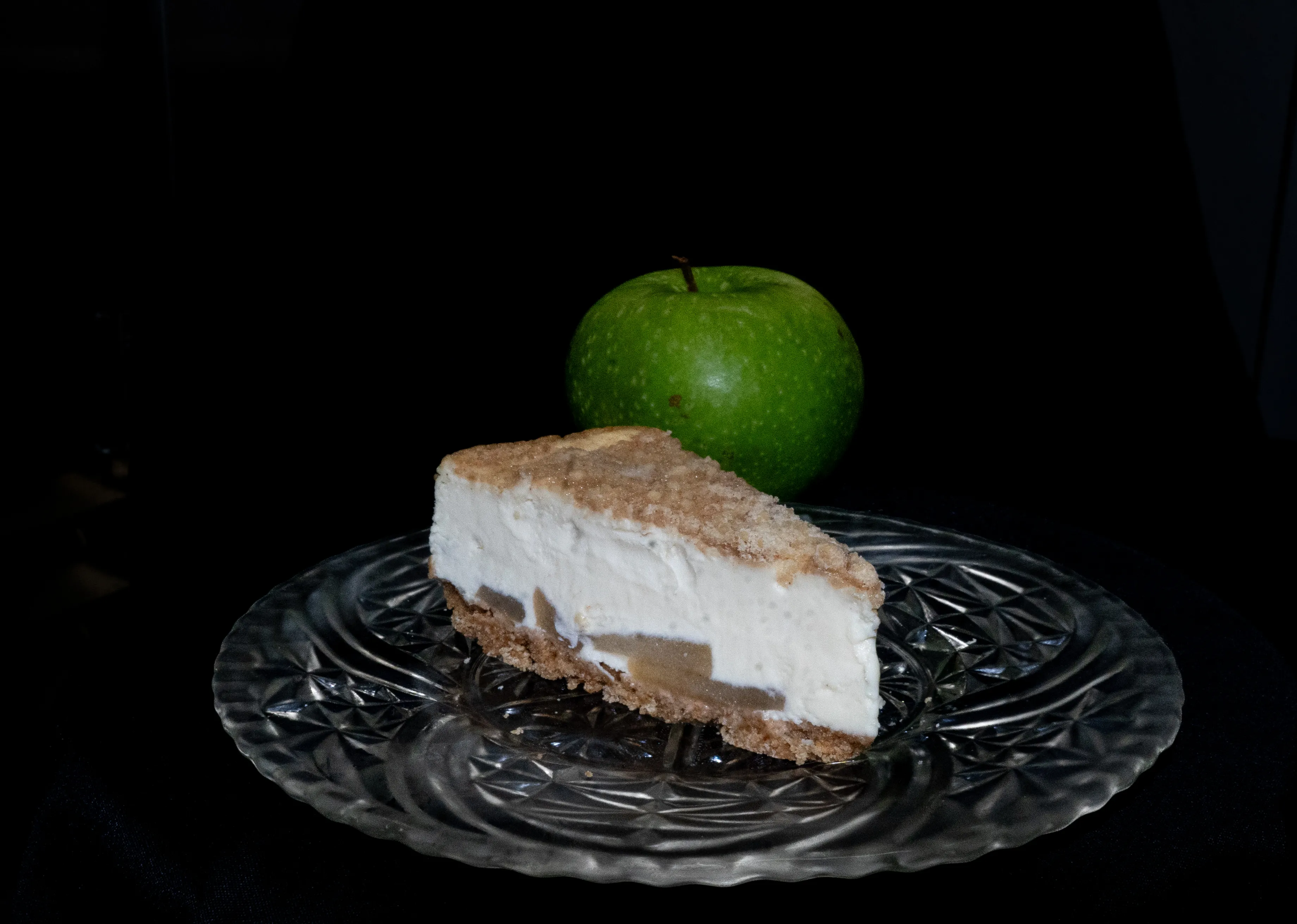 A slice of apple crumb pie sitting on top of a glass plate with an apple next to it