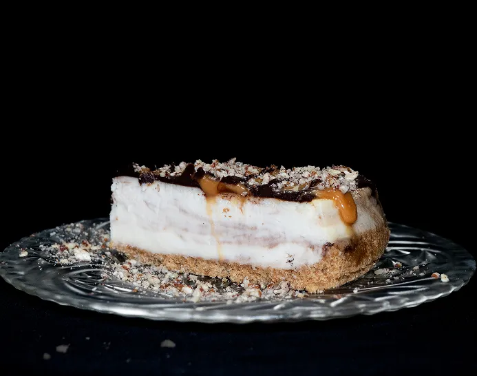 A slice of Turtle cheesecake with chocolate, peanut butter and coconut sitting on top of a glass plate