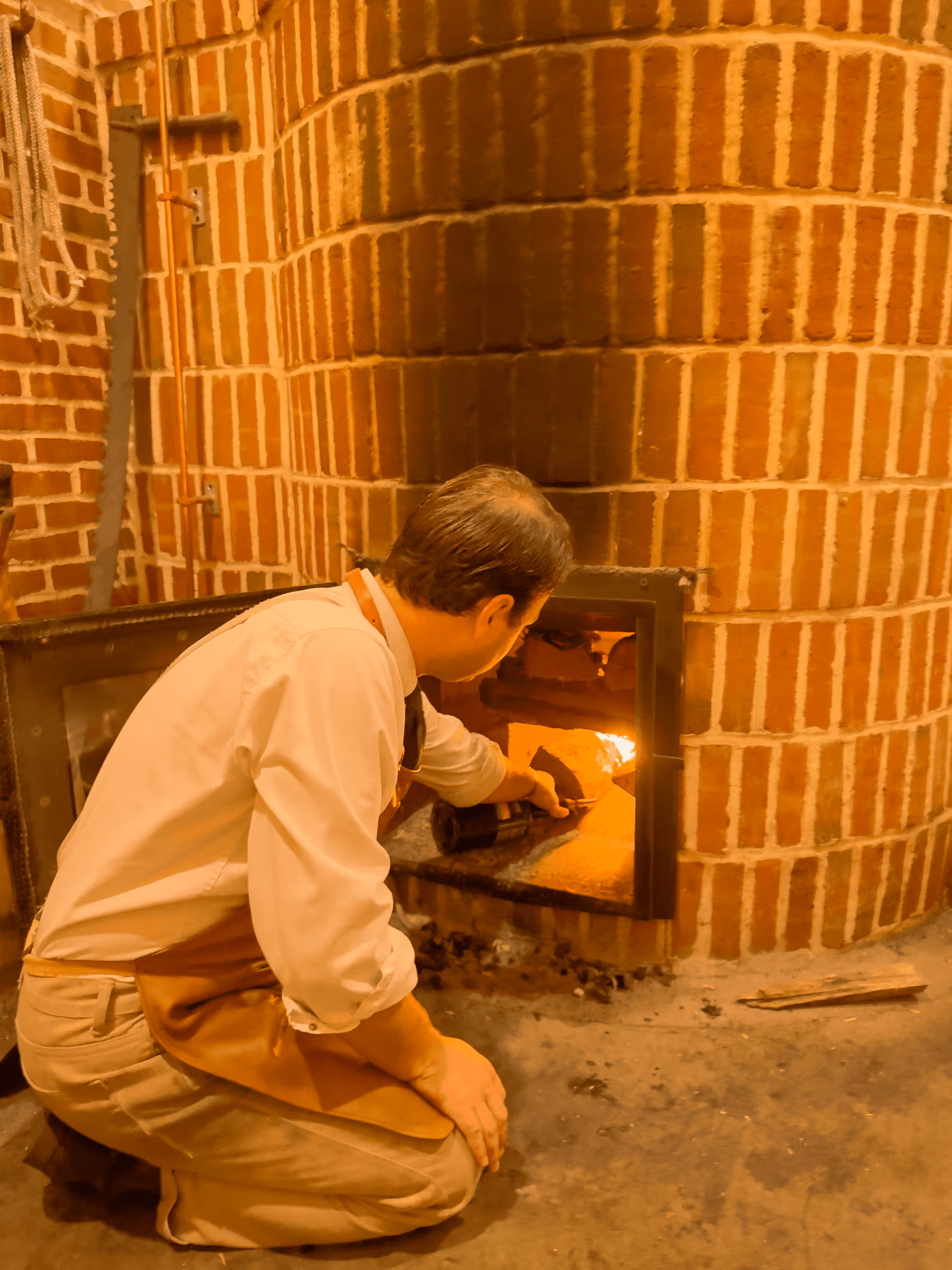 Baker tending to wood-fired oven surrounded by brick walls