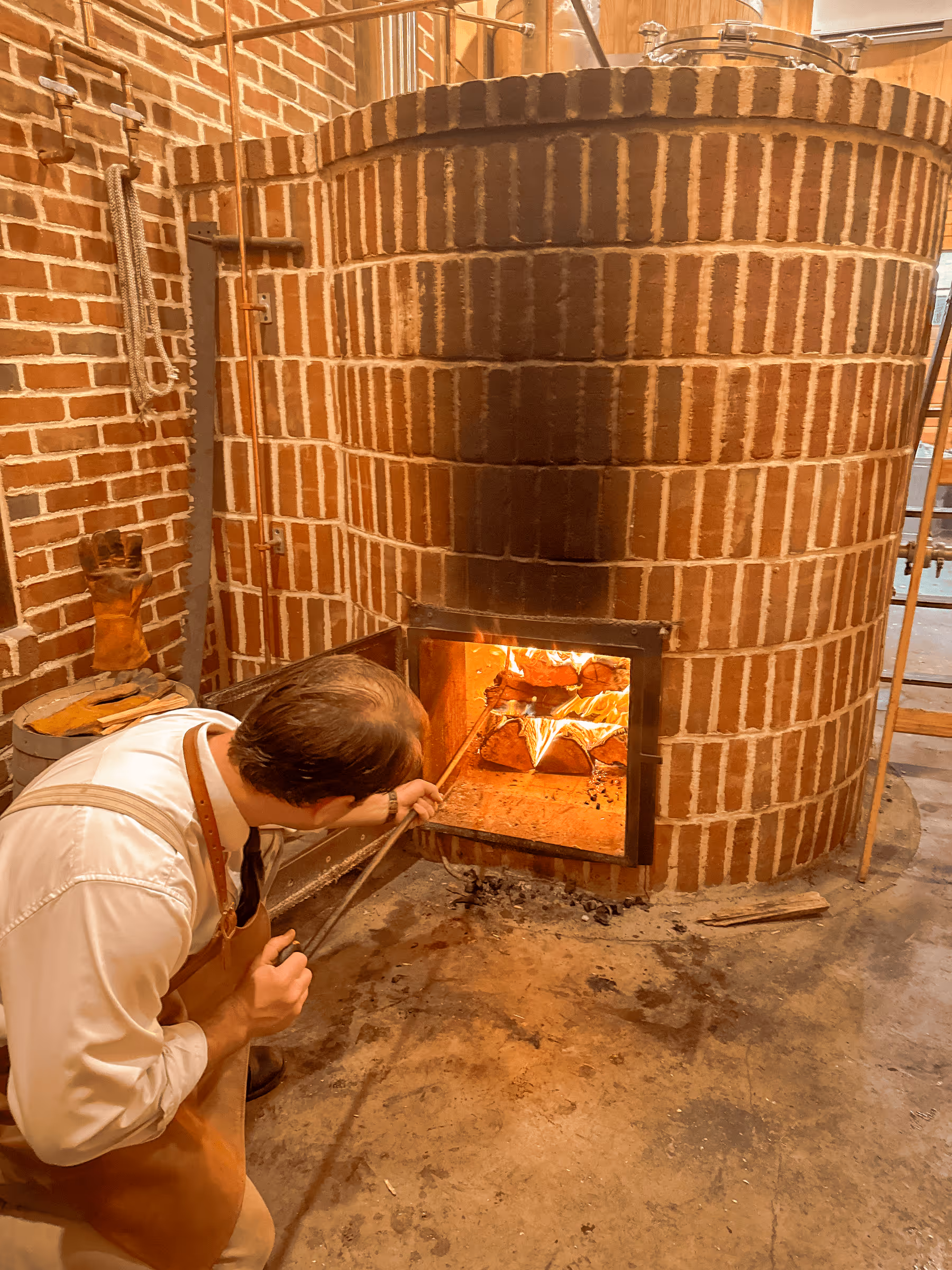 Baker stoking fire in large brick oven with glowing flames