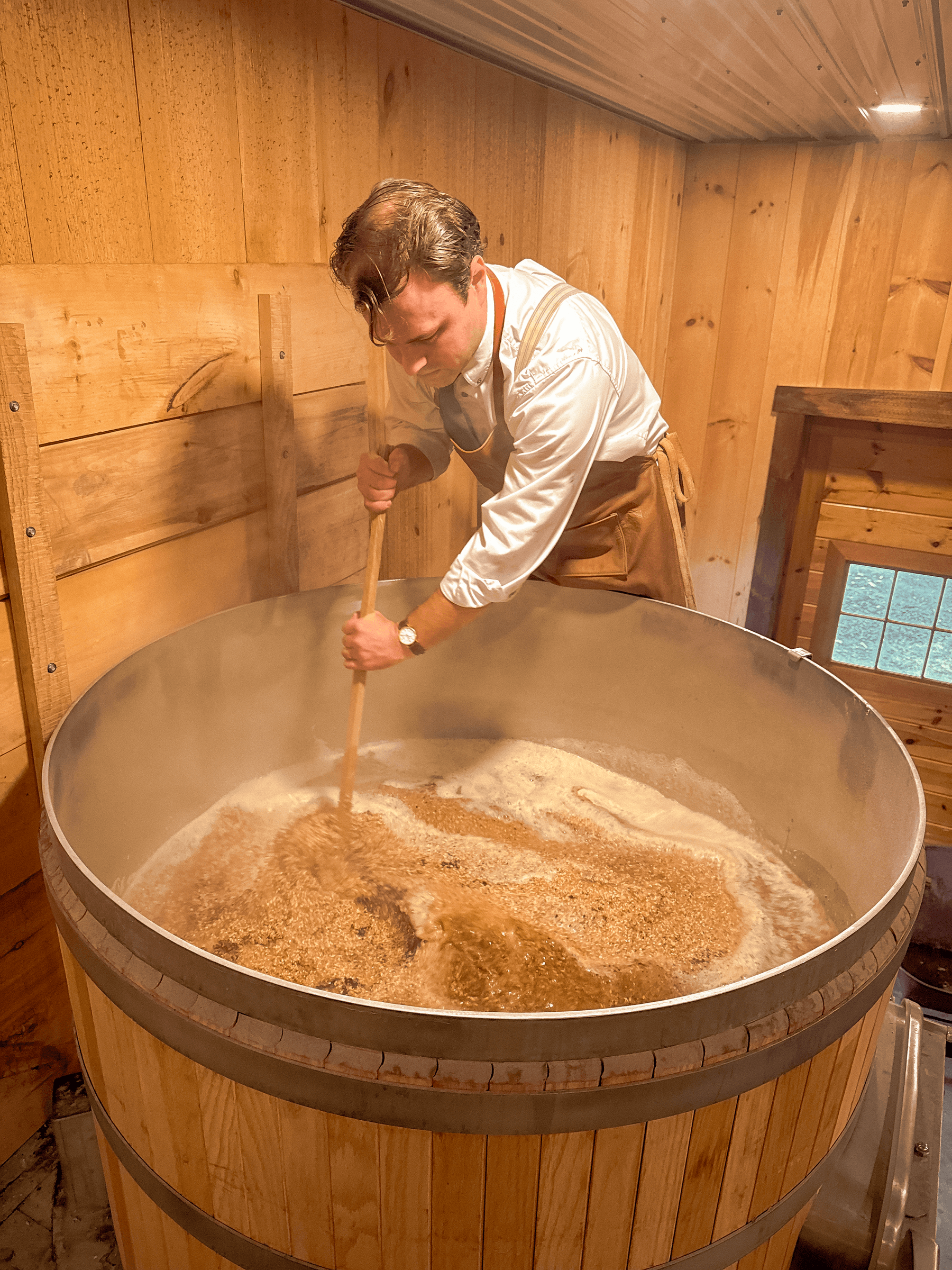 Brewer stirring large wooden brewing vat with grain and steam