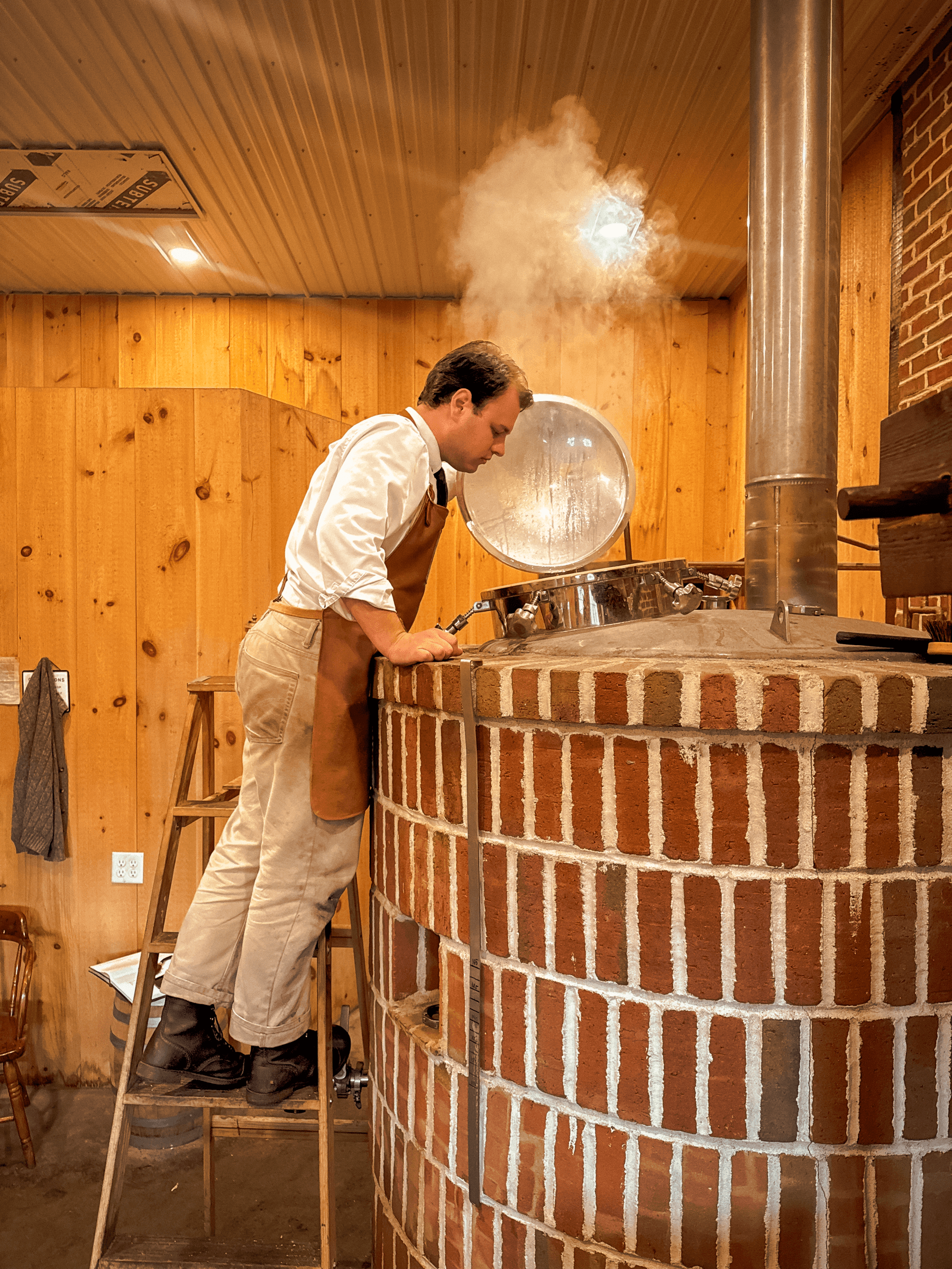 Chef standing on ladder cooking in brick wood-fired oven with steam