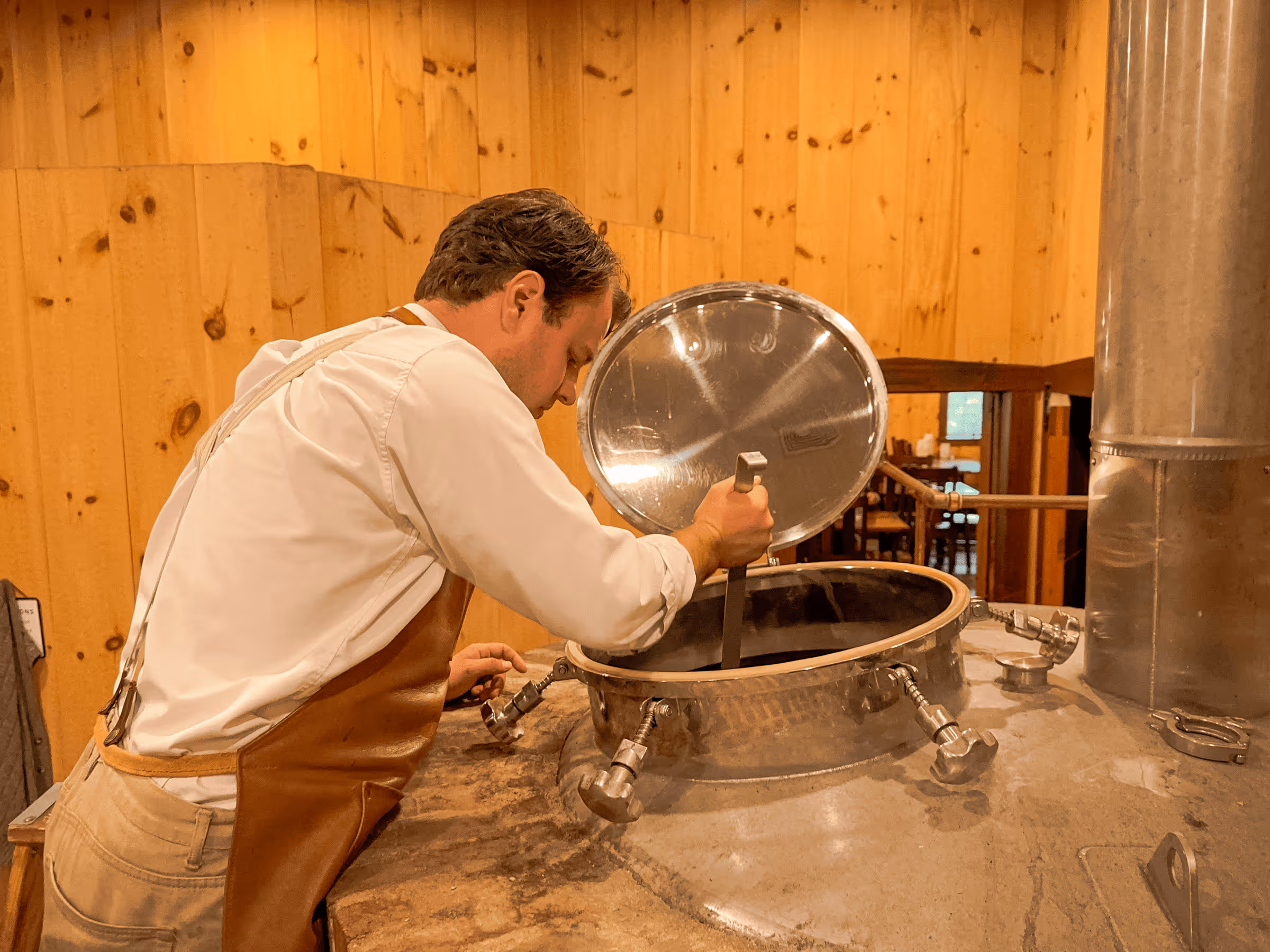 Brewer checking large metal brewing tank in wooden room