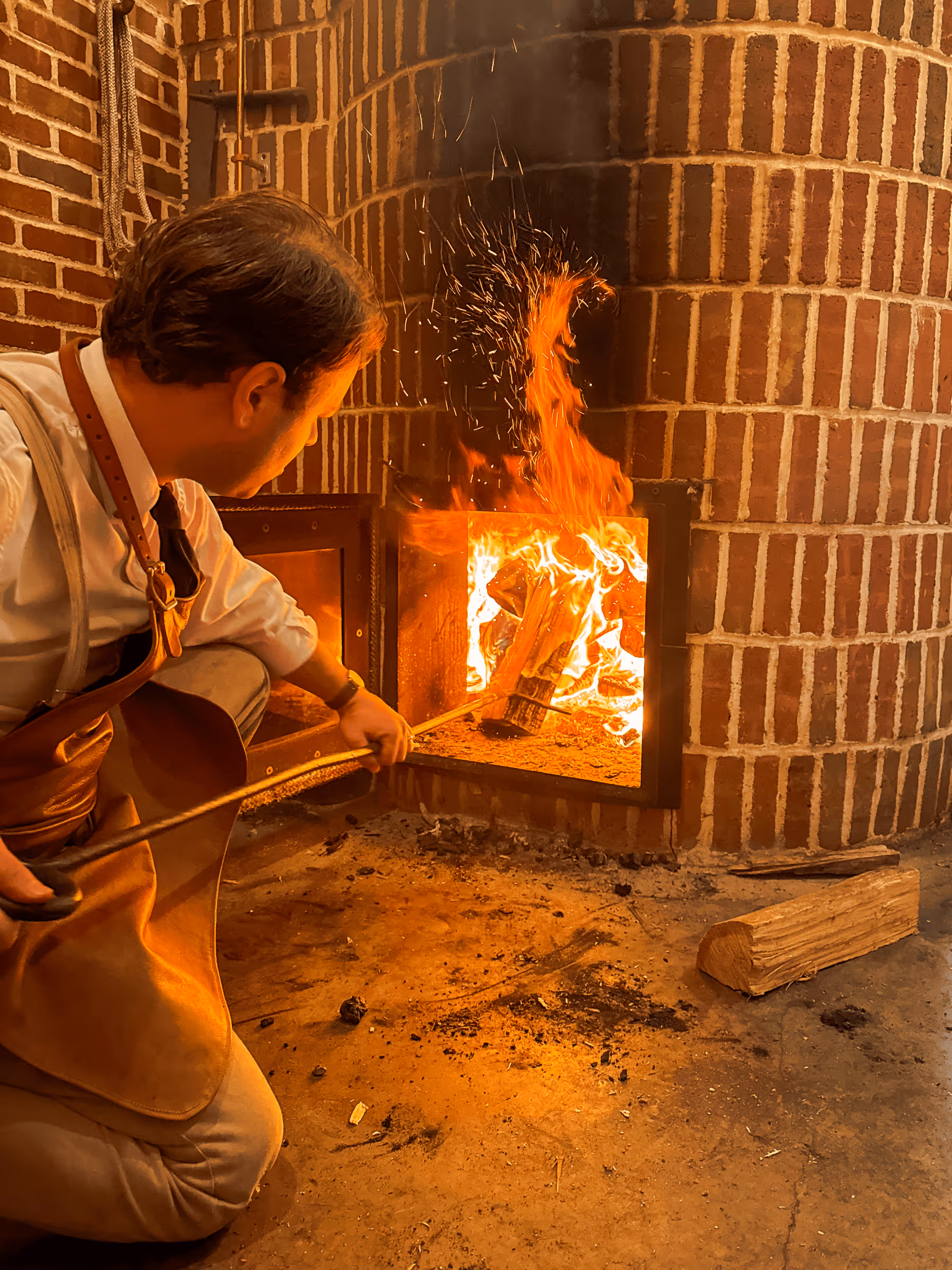 Baker tending to a roaring fire in a brick wood-fired oven
