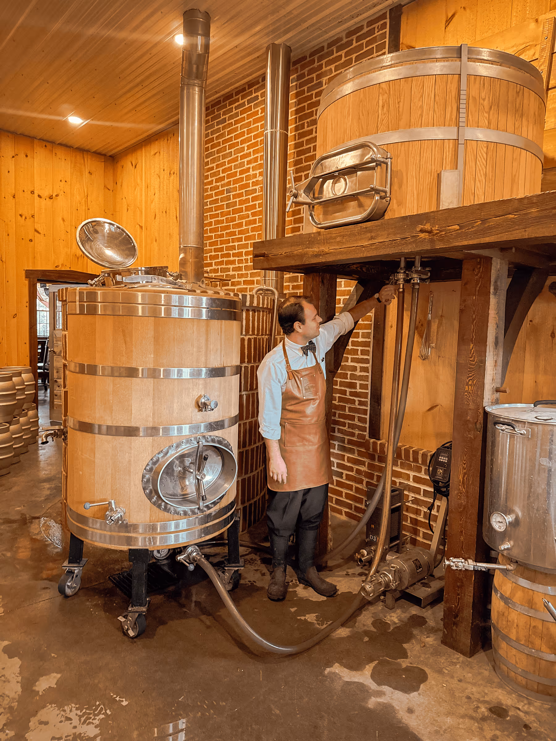 Brewer working in wooden craft brewery with large fermentation tanks