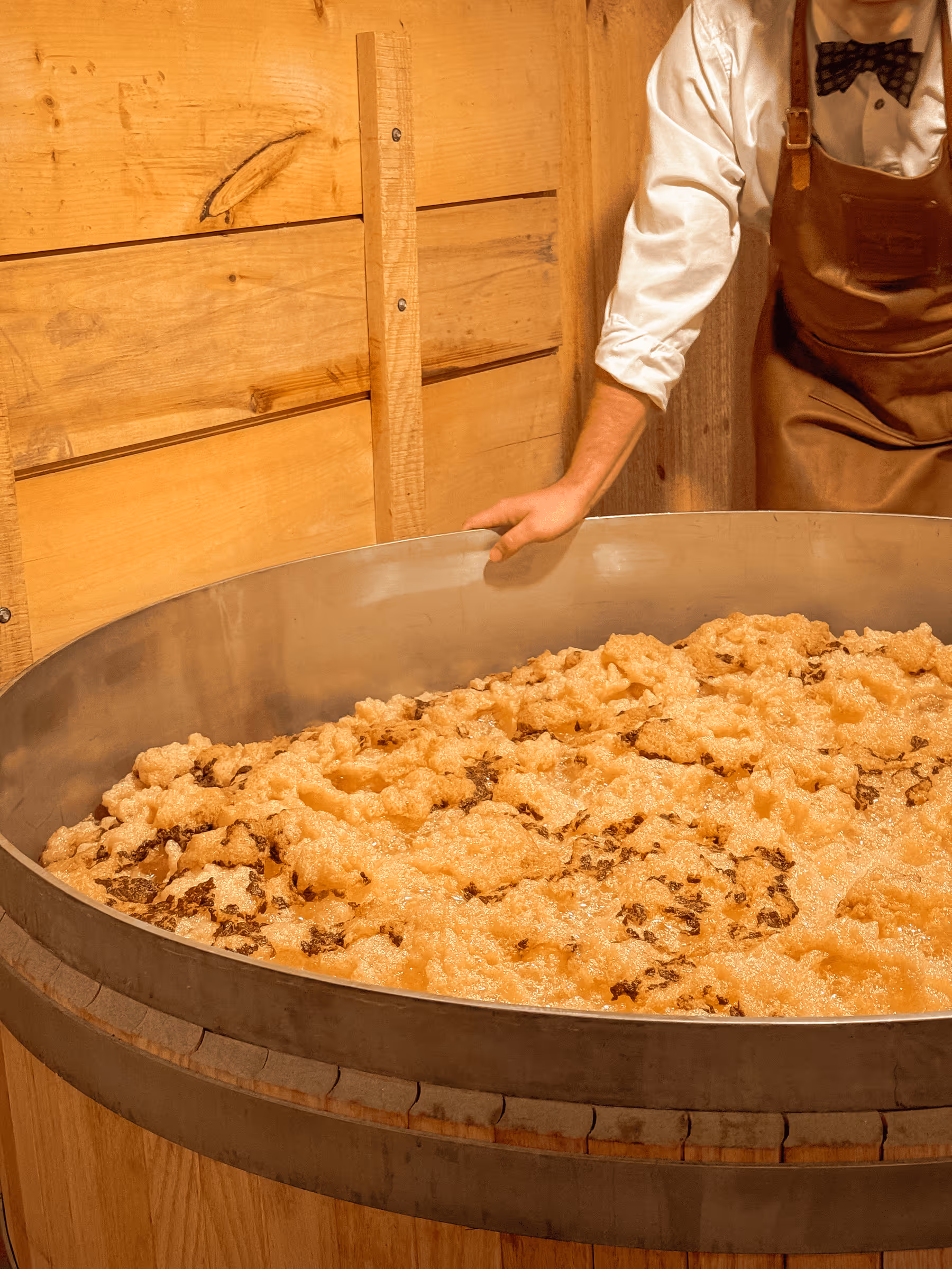 Baker mixing ingredients in large metal bowl with wooden background