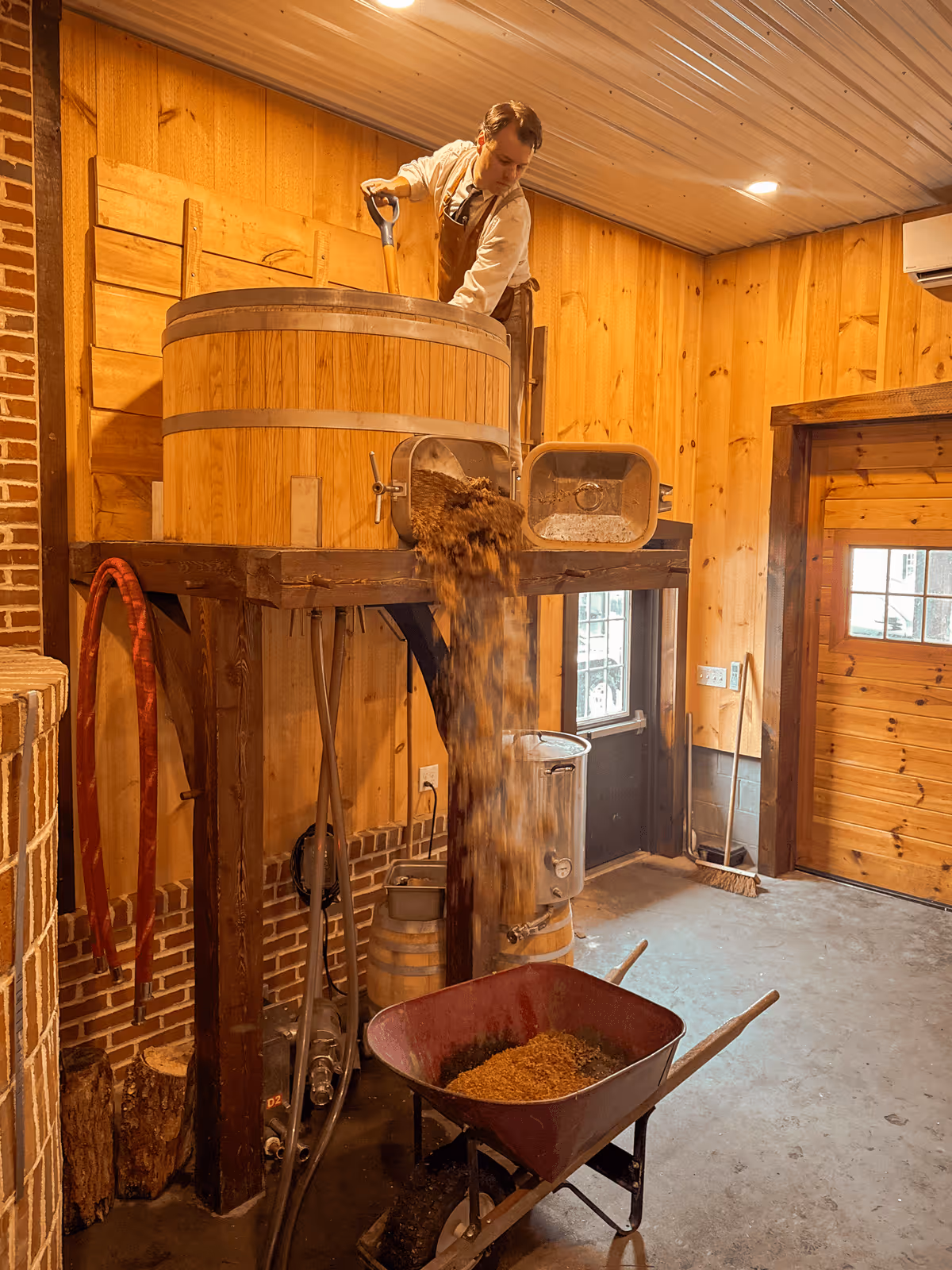 Wooden barrel brewery with grains being poured into a wheelbarrow