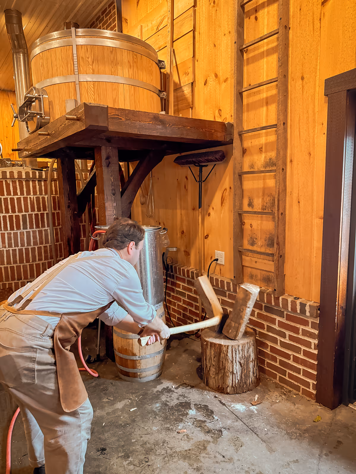 Craftsman chopping wood near brewing equipment in wooden workshop