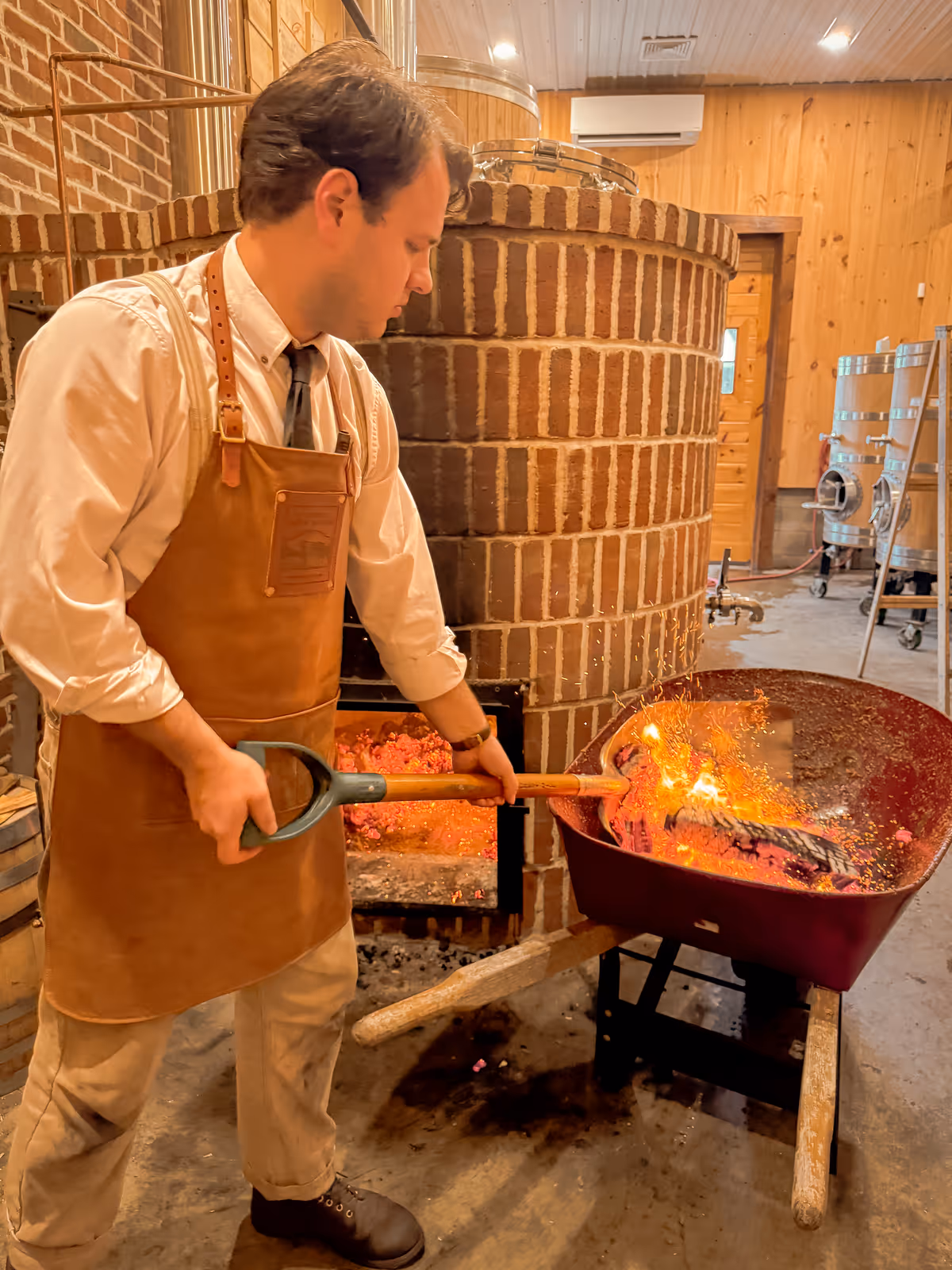 Craftsman working with hot embers near large brick kiln in workshop