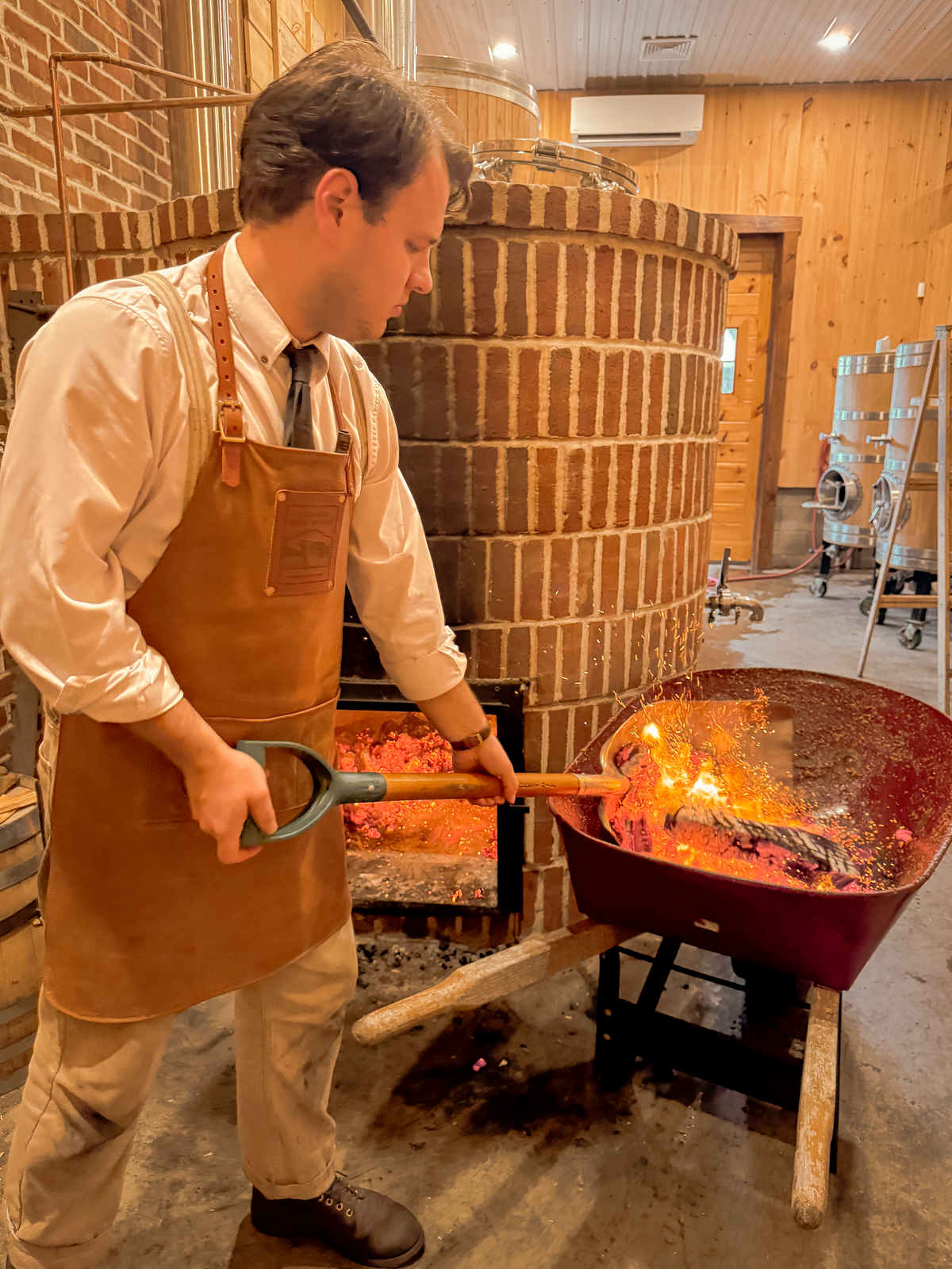 Craftsman working with hot embers near large brick kiln in workshop