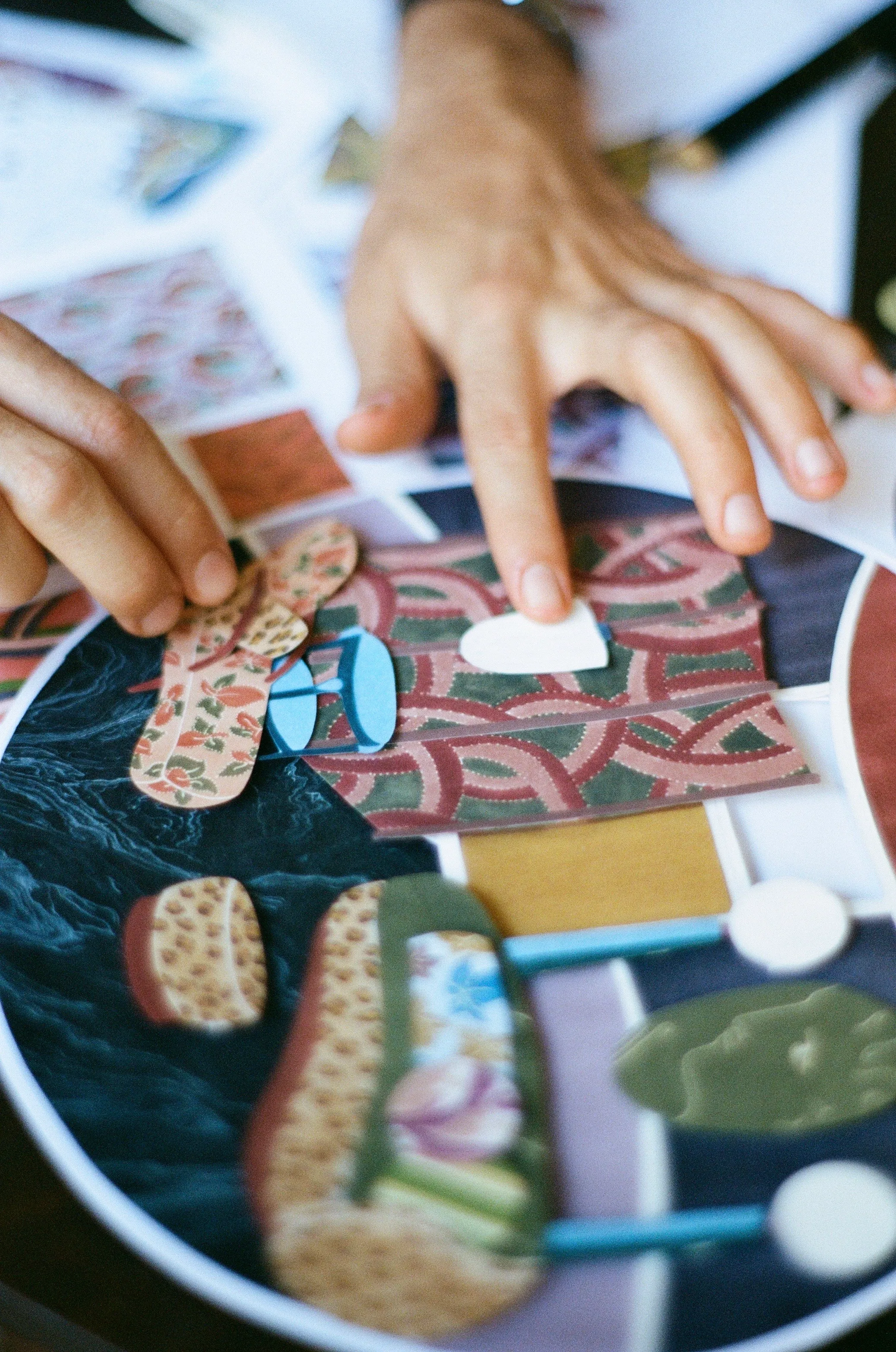Victor Cadène's hands assembling a paper collage of cut, hand-painted pieces
