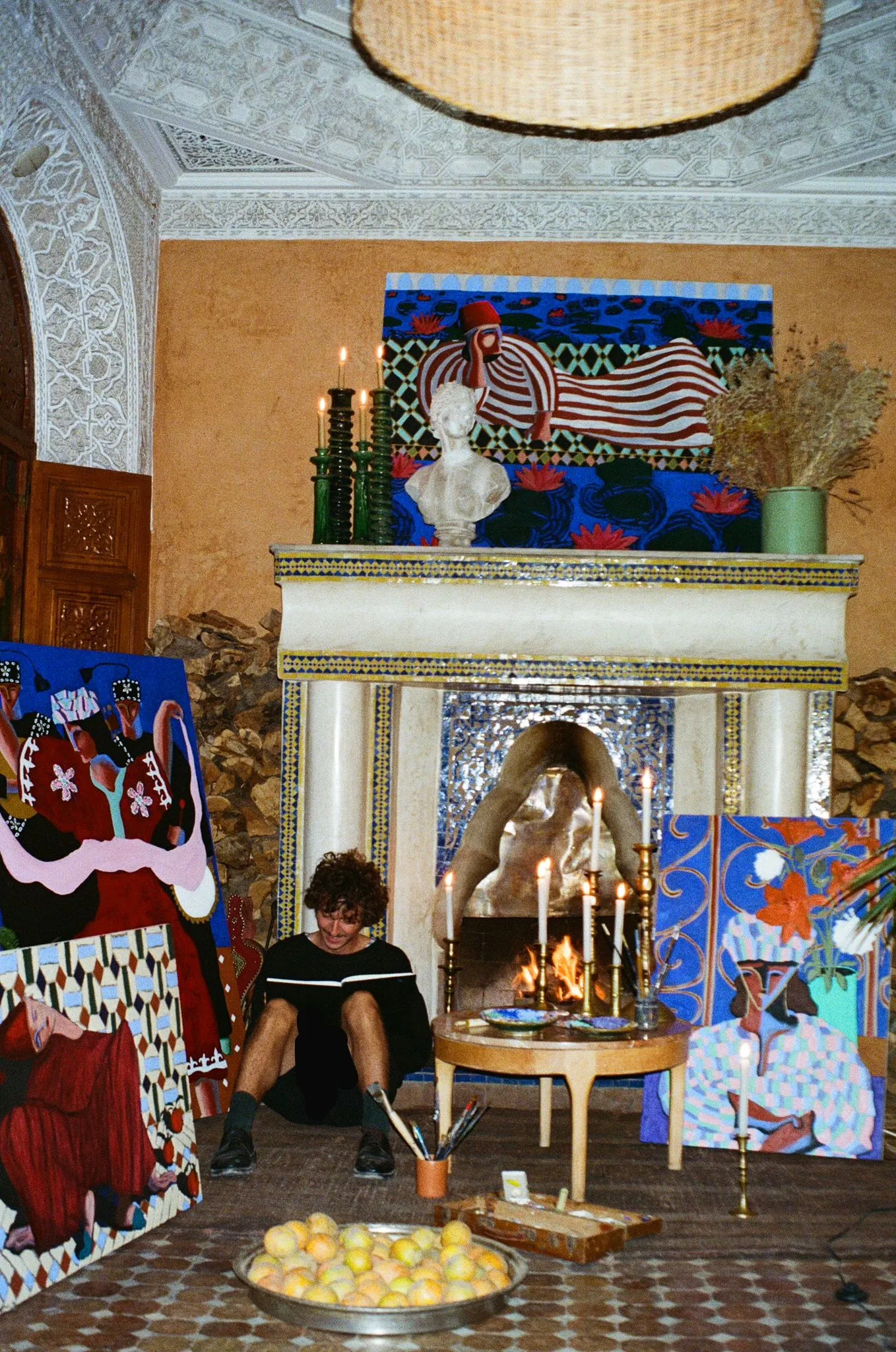 Paintings by Arsène Welkin arranged around a candlelit fireplace in a Marrakech riad