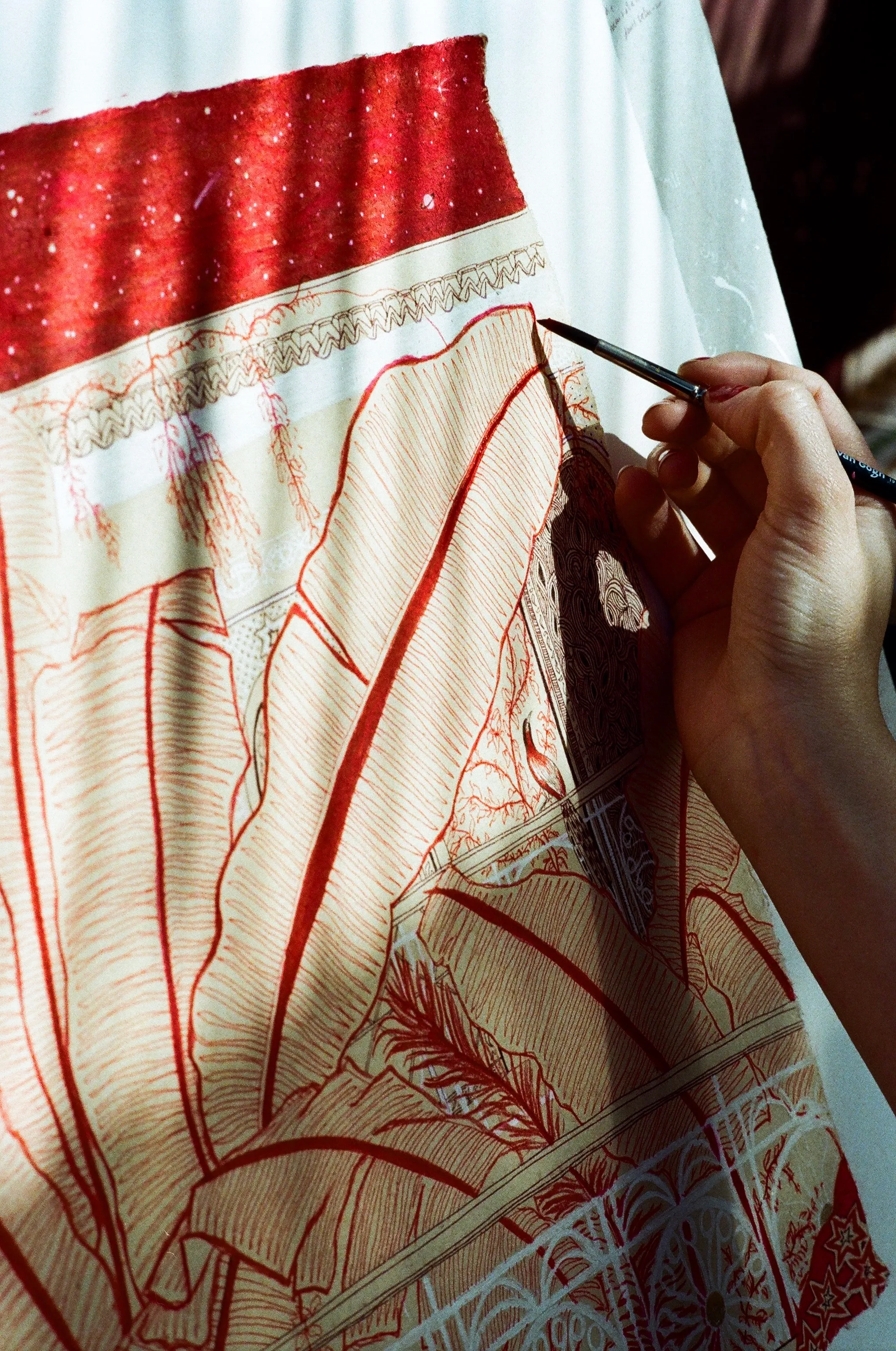 An artist's hand painting fine red palm leaves on a large textile, artist residency at Riad Jardin Secret