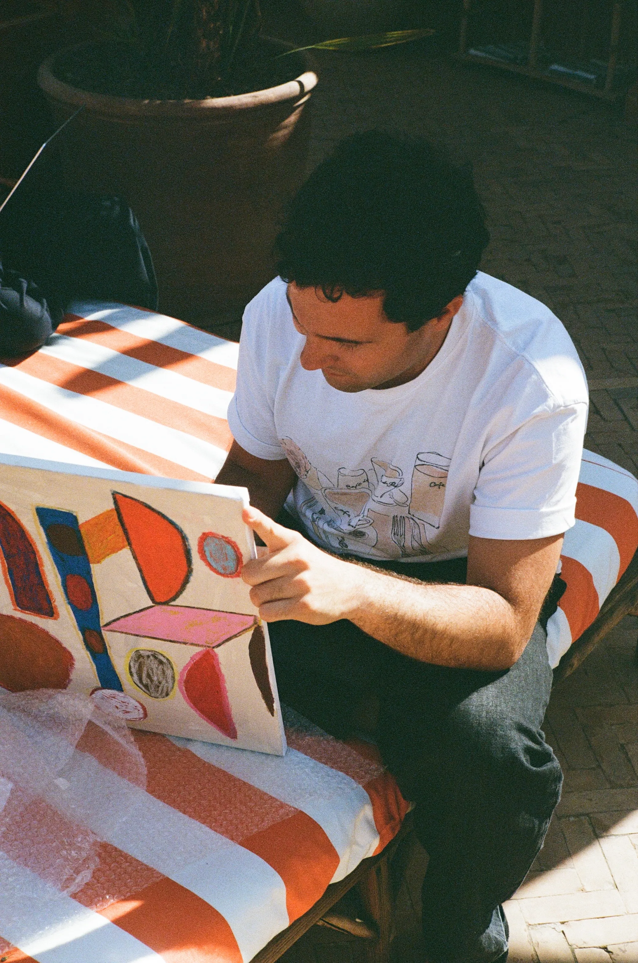 An artist examining a colourful painted work on paper in a sunlit Marrakech courtyard