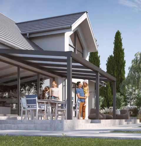 Familie mit zwei Kindern vor einem modernen weißen Haus mit grauem Dach und einer Terrassenüberdachung