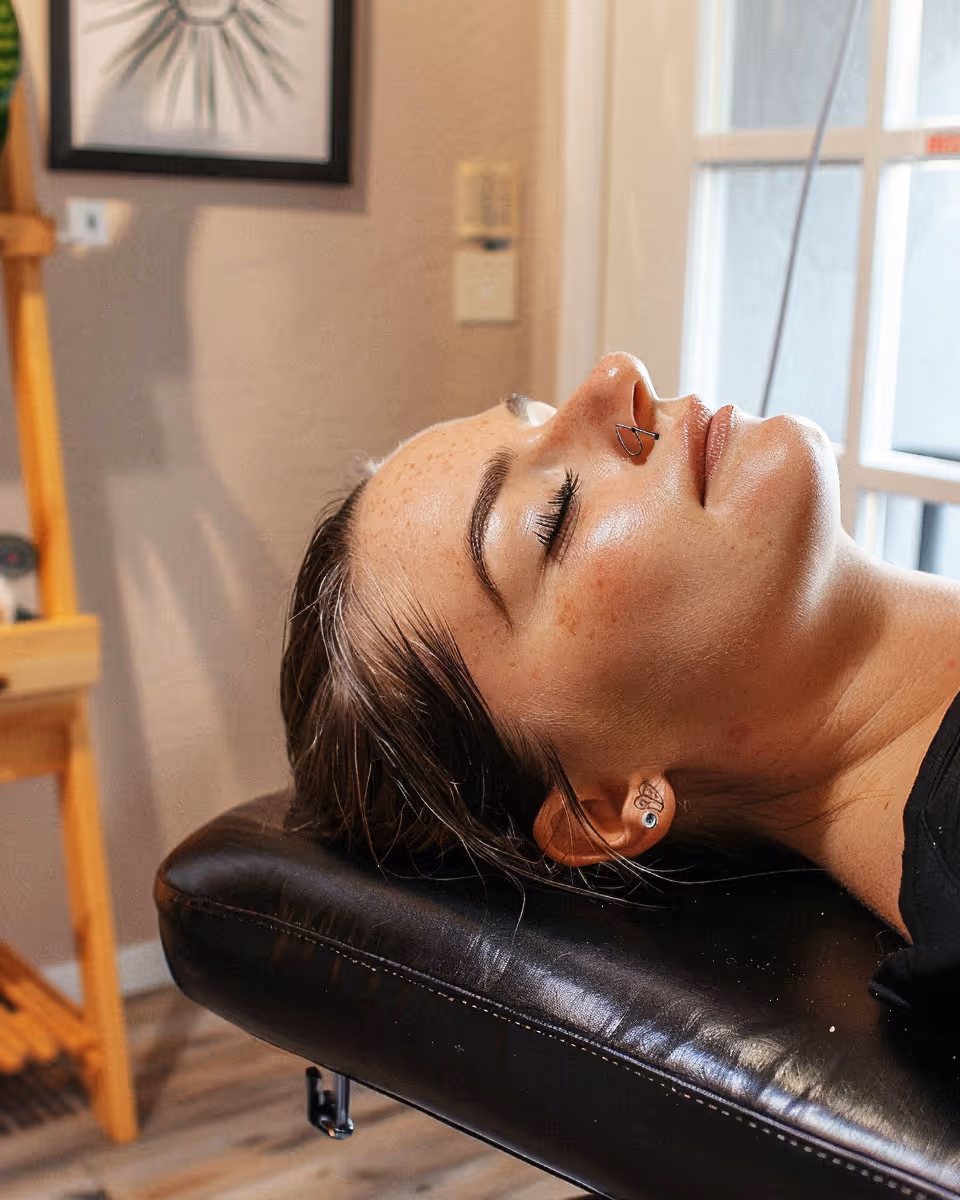Close-up of a woman with closed eyes resting her head on a black leather surface in a softly lit room.