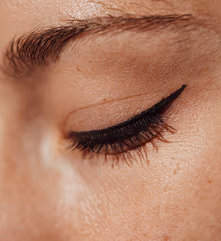Close-up of a closed eye with detailed natural skin texture and black winged eyeliner.