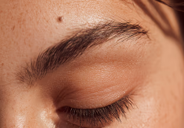 Close-up of a closed eye with long eyelashes and a well-groomed eyebrow on light skin.