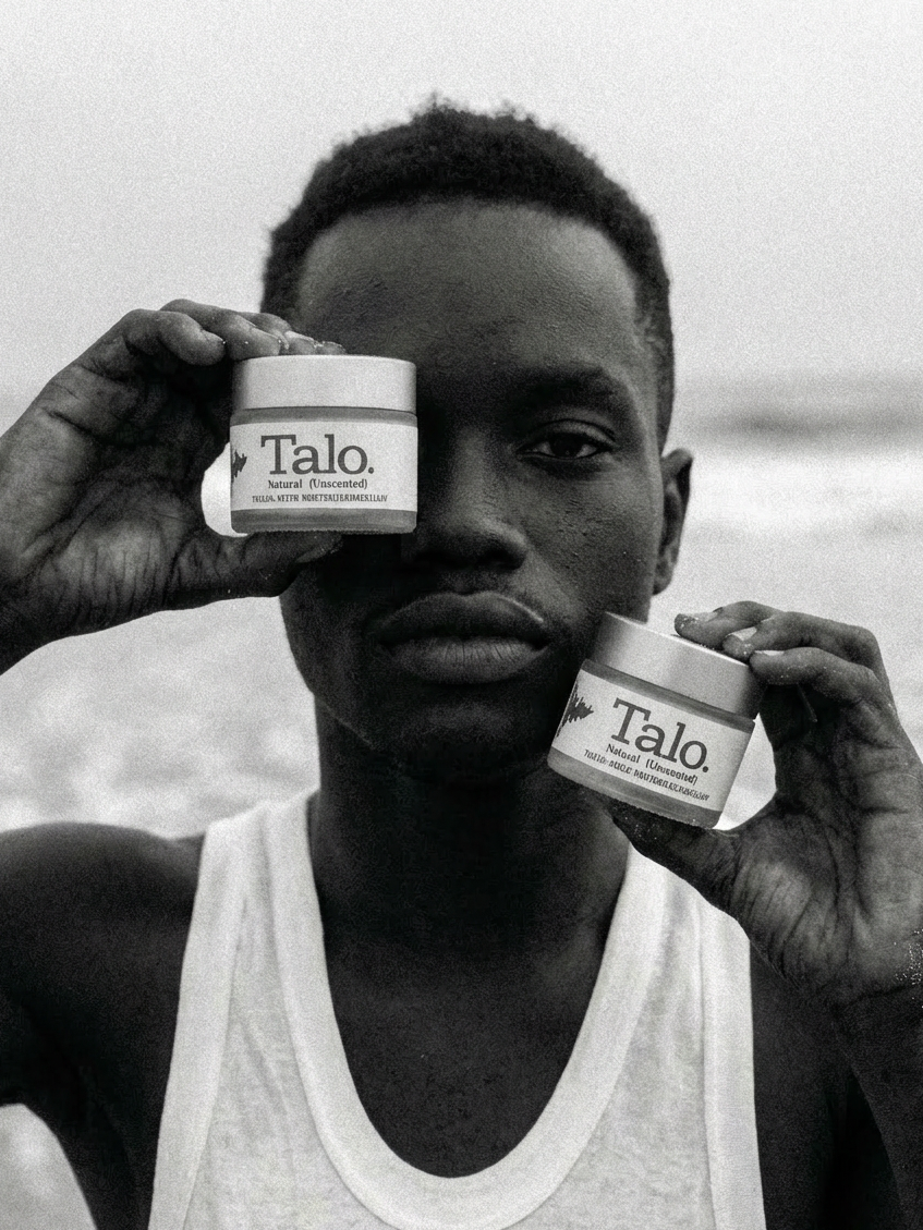 Man in white tank top holding two jars of Talo Natural (Unscented) skincare cream near his face.
