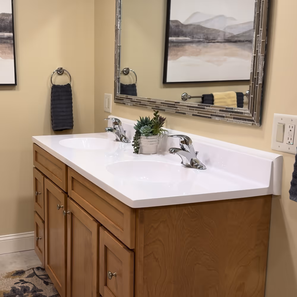 Bathroom vanity with double sinks, chrome faucets, wooden cabinets, and a rectangular mirror with mosaic tile border done by J&J Renovation