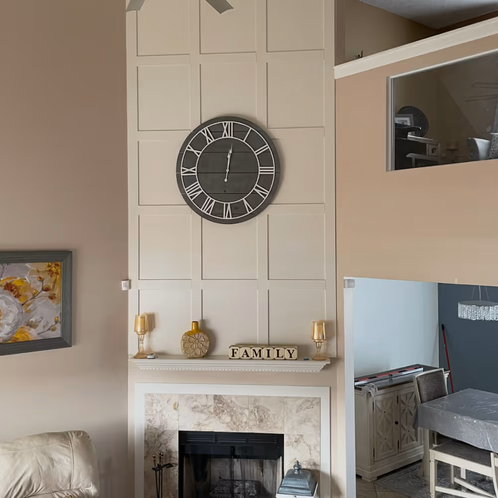 Living room fireplace with a large round black wall clock above it, decorative items, and wooden blocks spelling FAMILY on the mantel done by J&J Renovation