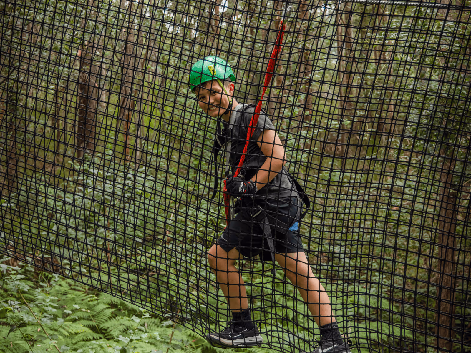 Smiling woman wearing safety helmet and harness walking on a rope bridge in at fSunshine Coast TreeTop Challenge Adventure Park