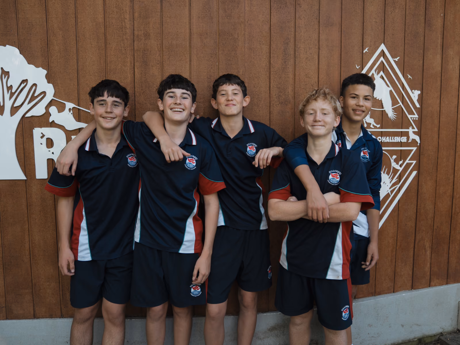 Five boys in matching sports uniforms standing with arms around each other smiling.