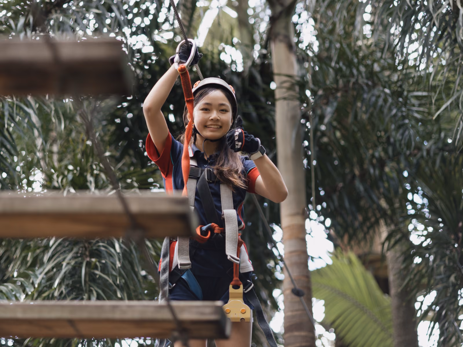 Young woman smiling and wearing safety harness and helmet on a treetop adventure course.