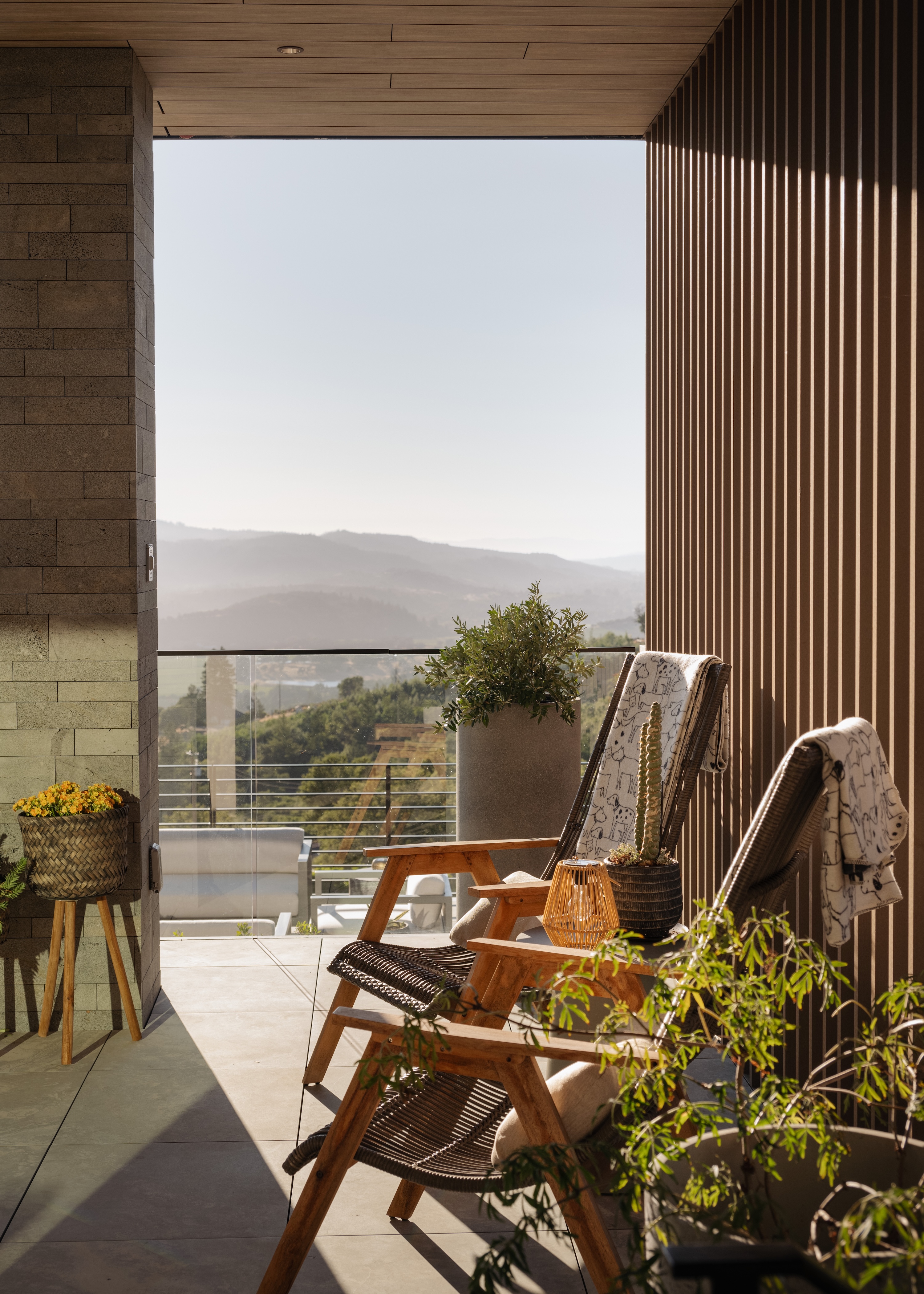 Two wooden lounge chairs with blankets on a balcony overlooking misty hills and green landscape.