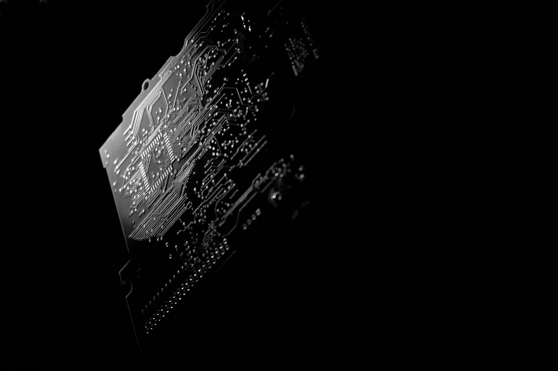 Close-up of a black circuit board with metallic traces and components lit against a dark background.