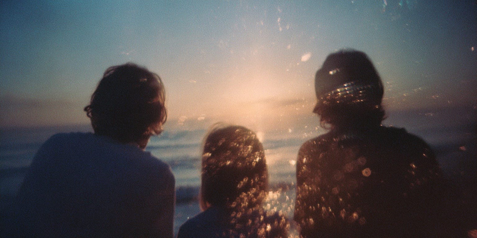 Three people viewed from behind watching a sunset over the ocean with light reflections around them.